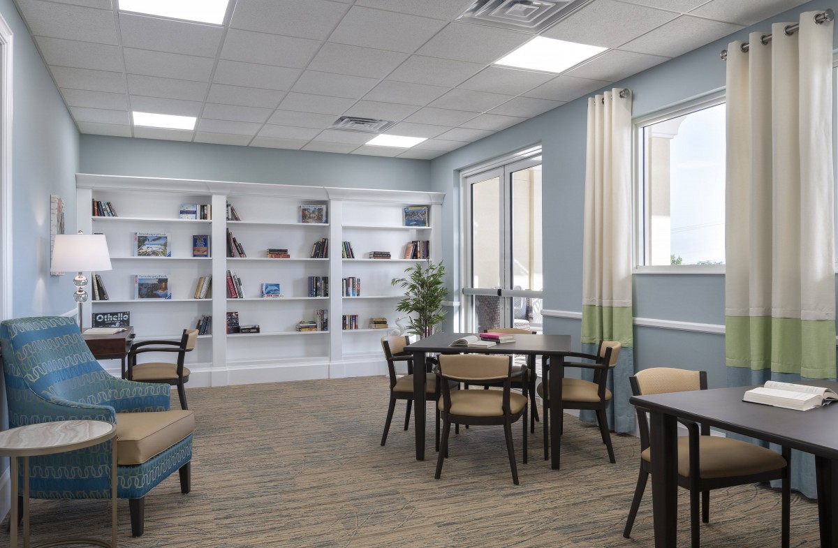 A modern library interior with bookshelves, tables, and chairs under bright lighting.