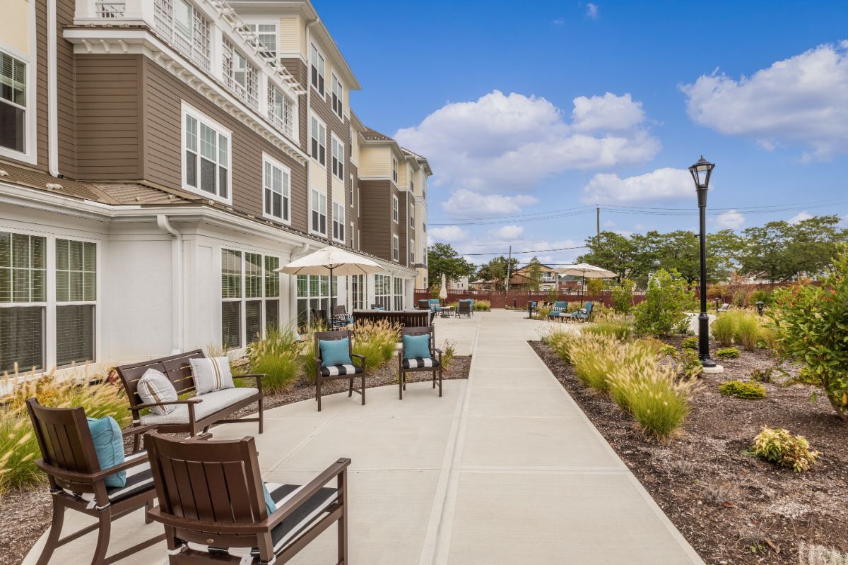 A well-maintained sidewalk with outdoor seating at a residential complex under a clear blue sky.