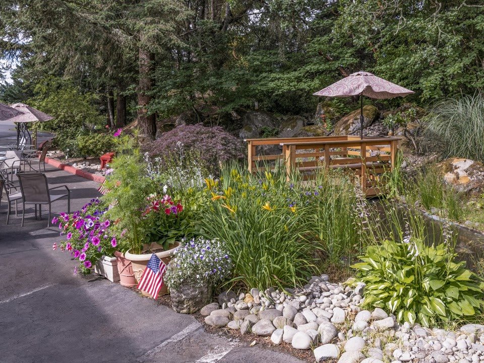 A beautifully landscaped garden featuring a variety of flowers, a rock garden, and an inviting outdoor seating area with a patio umbrella.