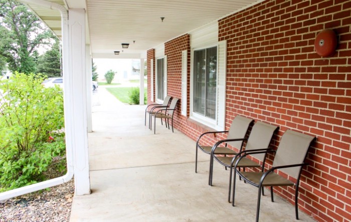 A covered porch with several chairs lined up against a brick wall.