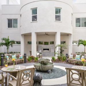 A modern building with a central courtyard featuring a fountain and outdoor seating surrounded by lush landscaping and palm trees.