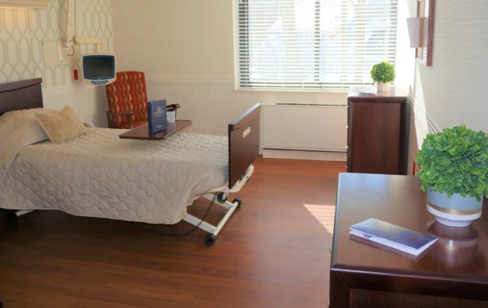 A hospital room with a single bed, bedside table, and a window allowing natural light in.