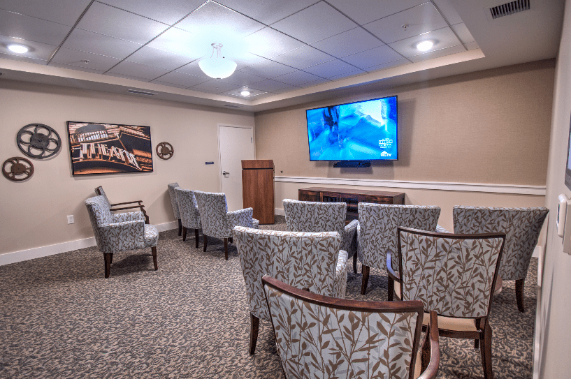 A small conference room with patterned chairs facing a large wall-mounted television.
