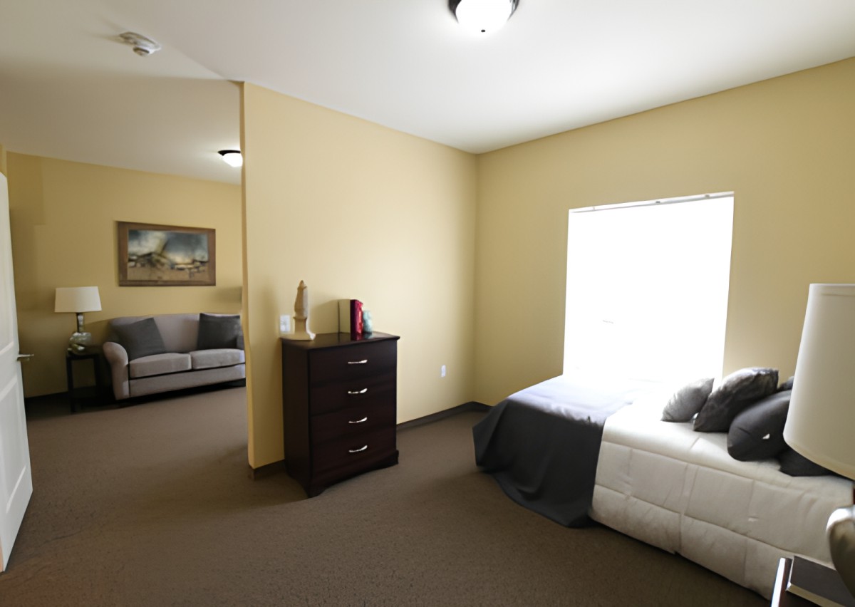 A view of a bedroom with a dresser, bed, and sofa in the adjoining room.