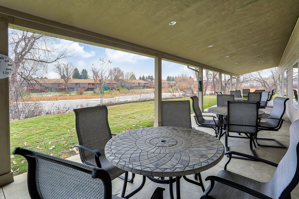 A covered patio with metal tables and chairs overlooking a grassy landscape on a sunny day.