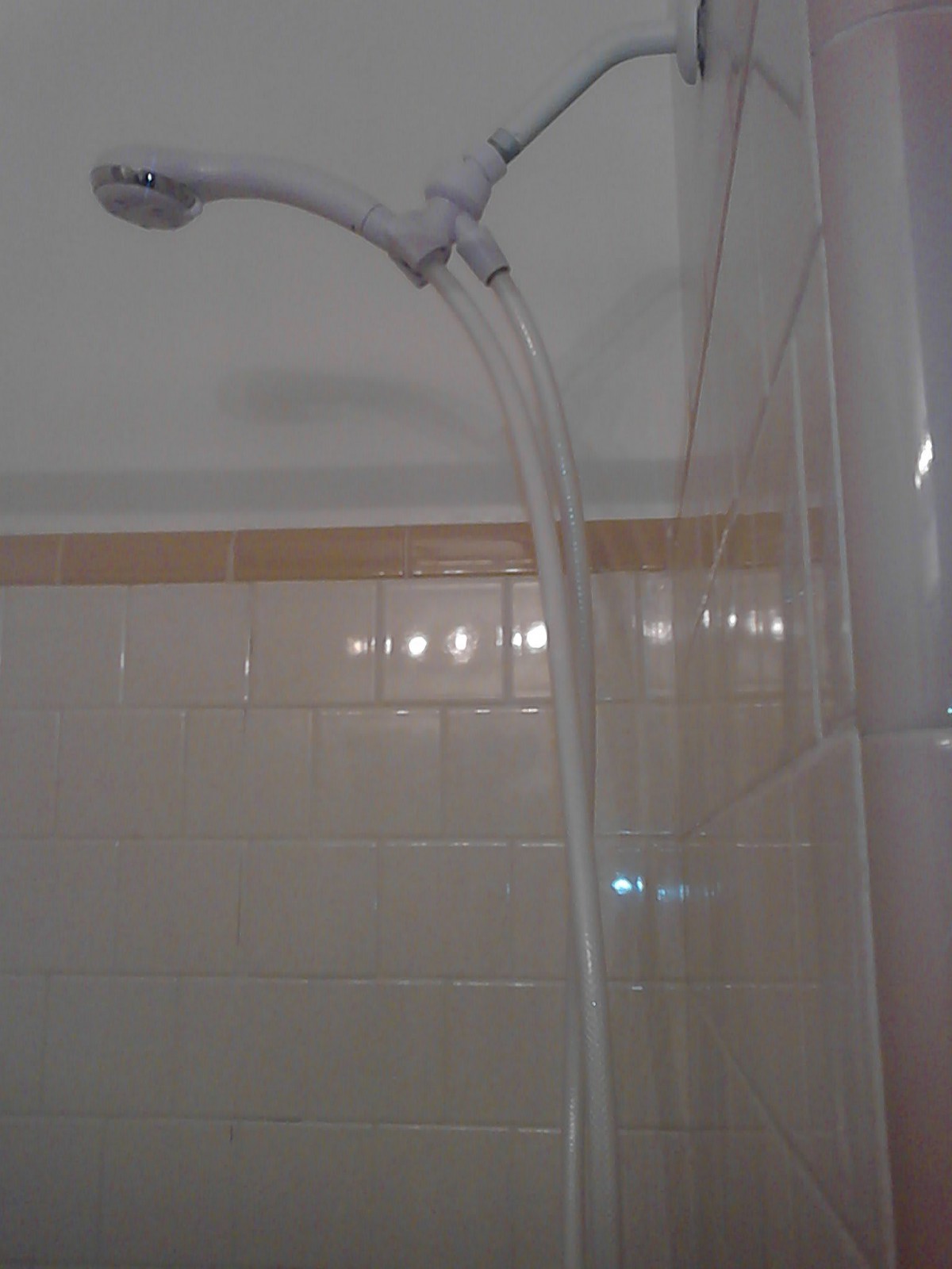 A shower with a handheld showerhead and tiled wall in a bathroom.