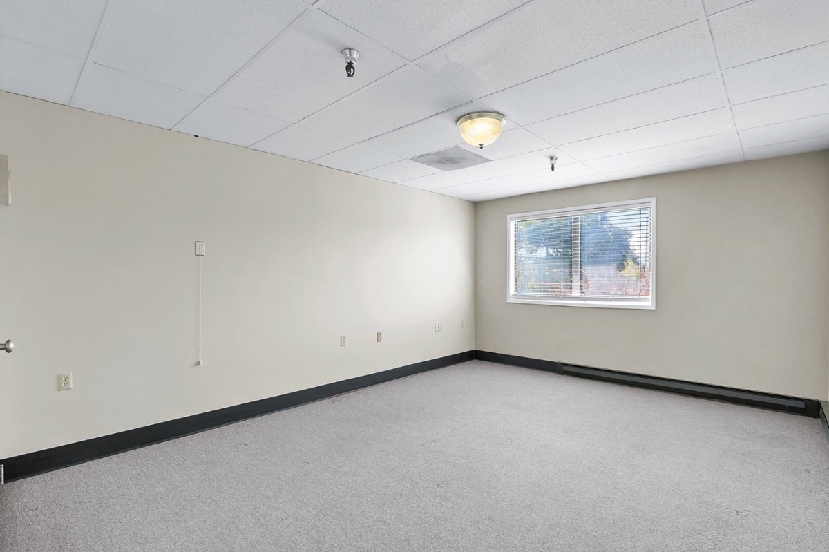 An empty office room with a window and carpeted flooring.