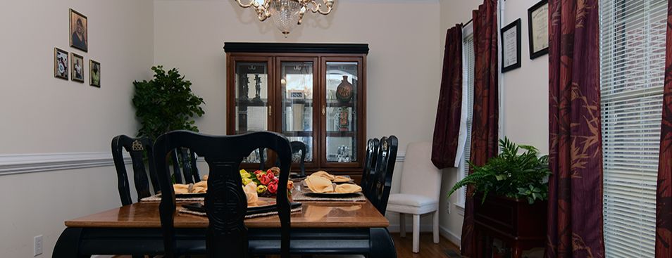 A cozy dining room with a wooden table set, surrounded by black chairs and complemented by a glass cabinet and chandelier.
