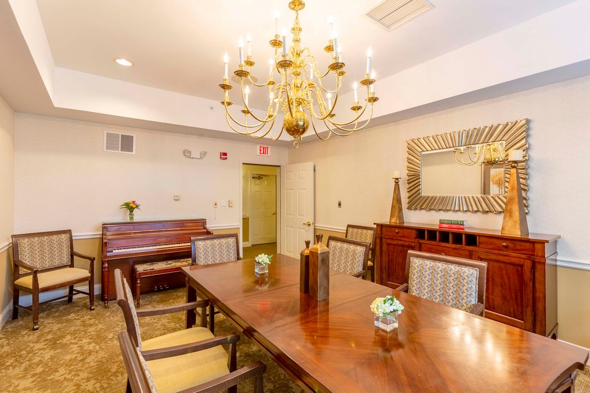 A well-appointed dining room featuring a large wooden table, elegant chandelier, and a piano in the corner.