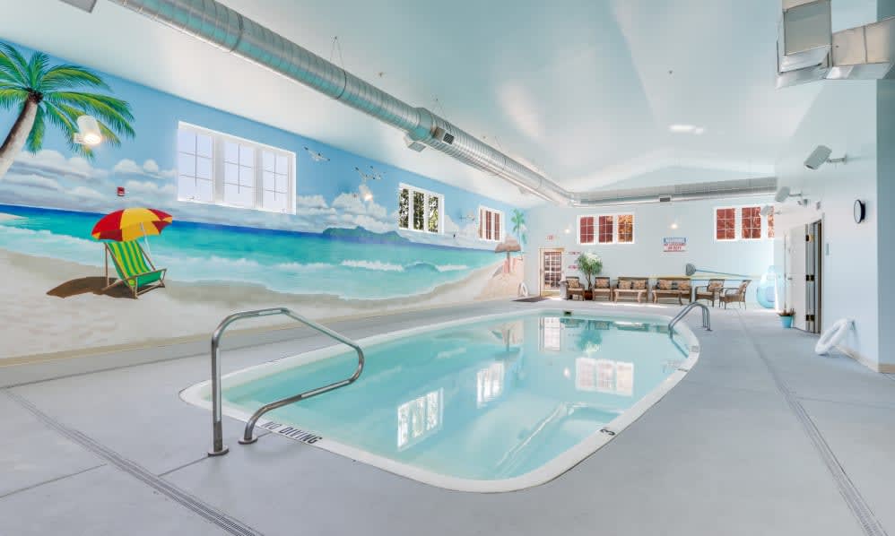 An indoor swimming pool with a beach-themed mural on the wall.