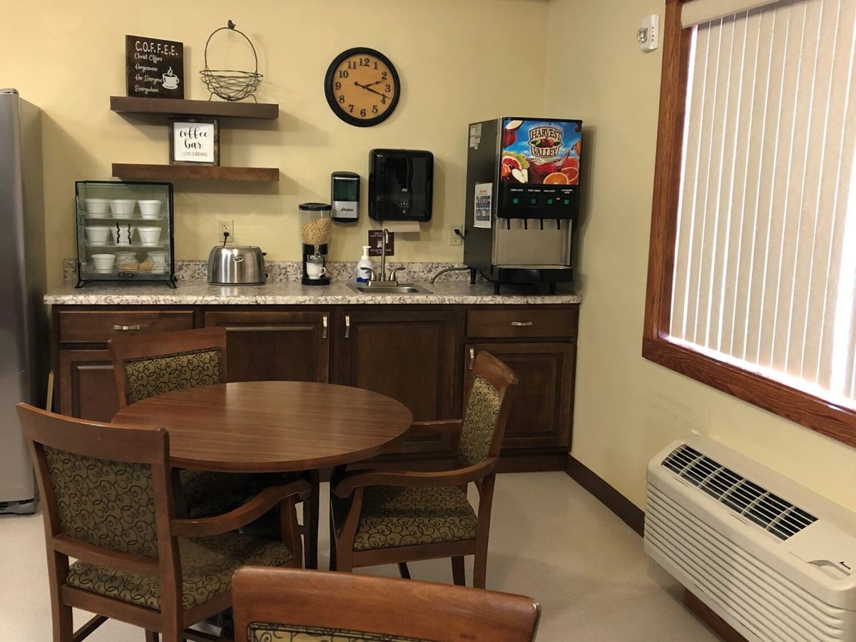 A cozy break room with a coffee station, beverage machine, and a round table with chairs.