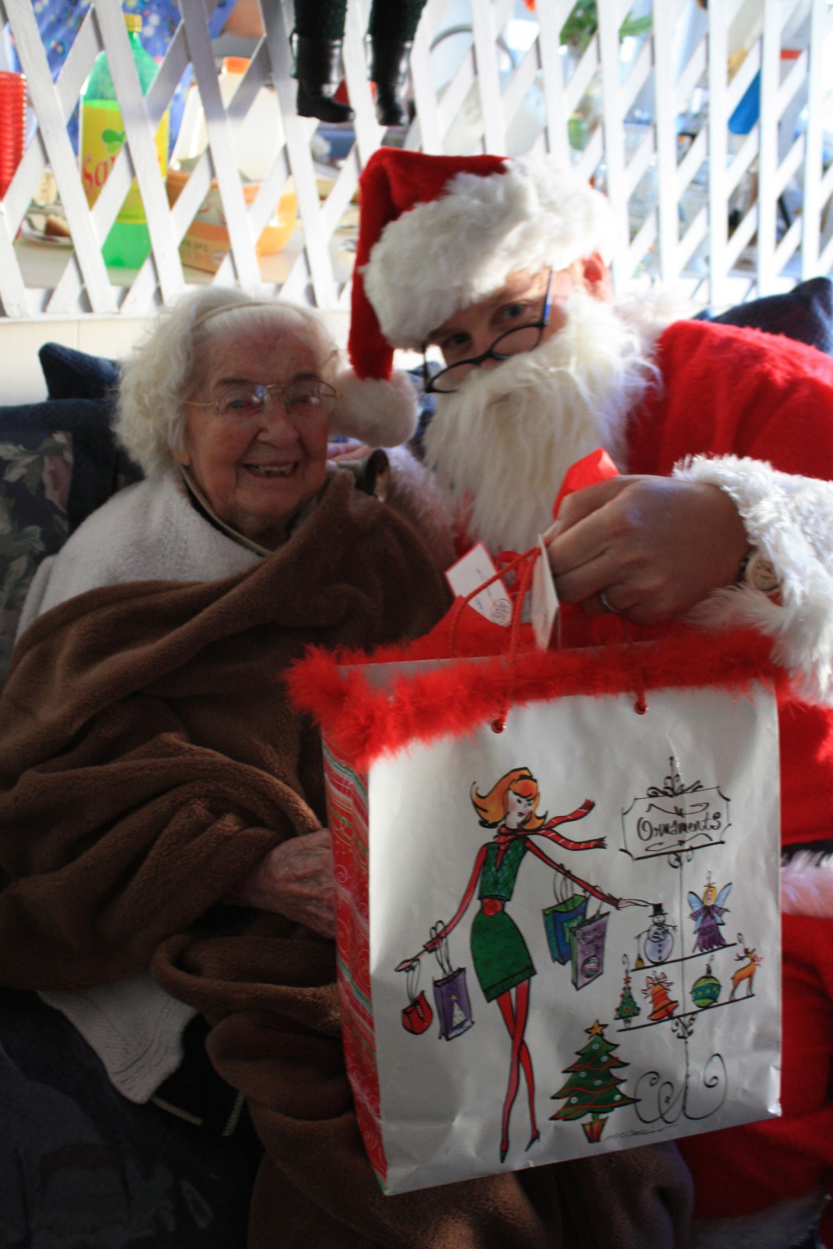 An elderly woman smiles while receiving a gift from Santa Claus.