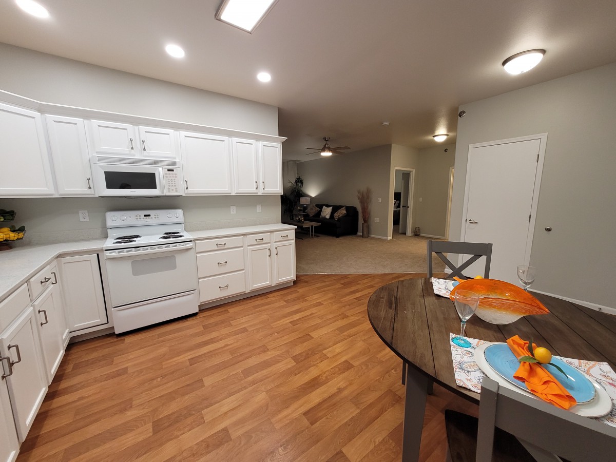A modern kitchen with white cabinets and an adjacent dining area, featuring wood flooring and an open layout.
