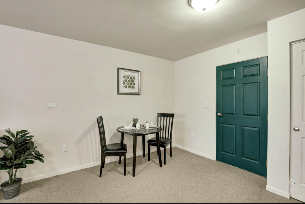A minimalist dining area with a small table and two chairs, complemented by wall art and a green door.