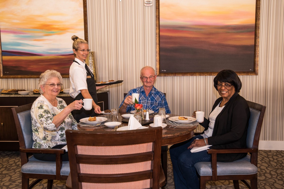 A group of elderly people enjoying a meal at a restaurant with a server assisting them.