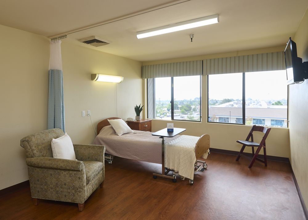A clean and spacious hospital room with a patient bed and large windows.