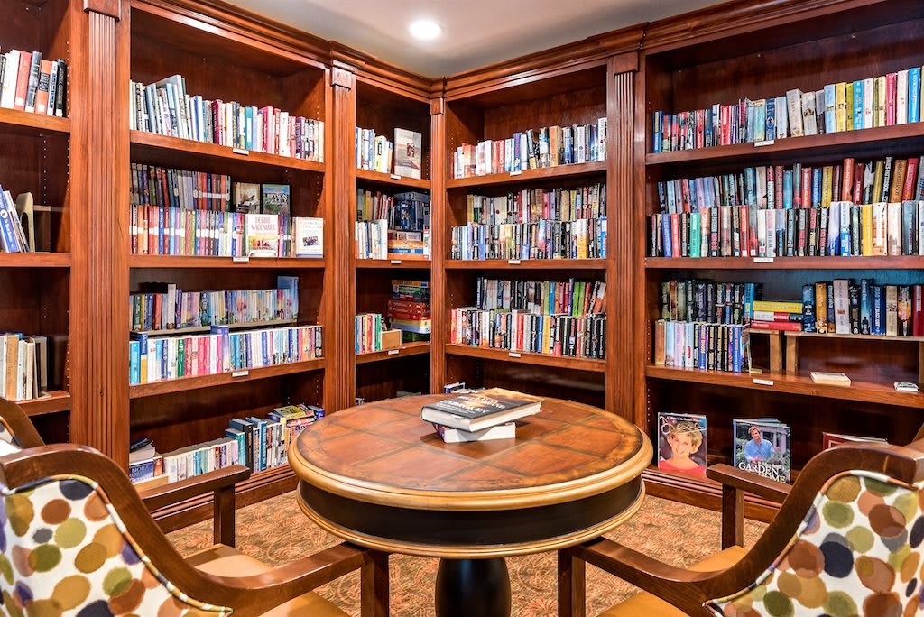 A cozy library corner with wooden shelves, a round table, and chairs.
