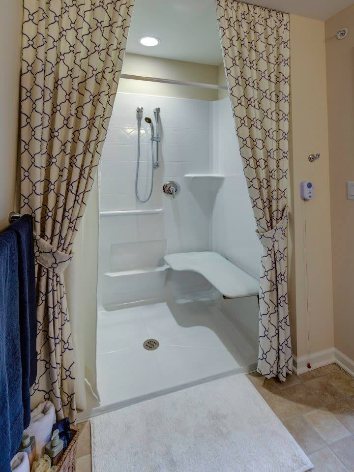 An accessible shower with a seat and handrails, enclosed by patterned curtains.