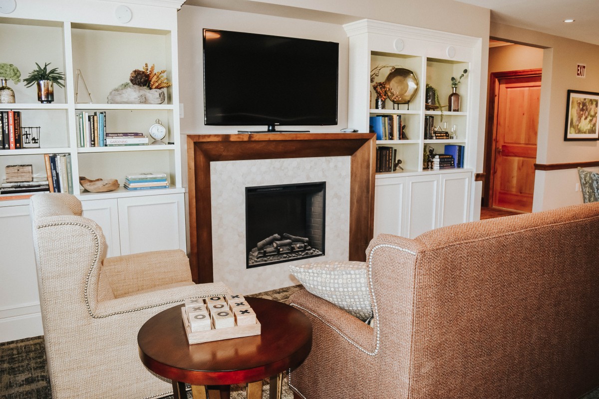 Cozy living room with a fireplace and TV, surrounded by bookshelves and comfortable seating.