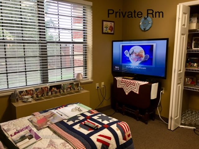 A cozy private bedroom featuring a quilted bed and a television under a window.