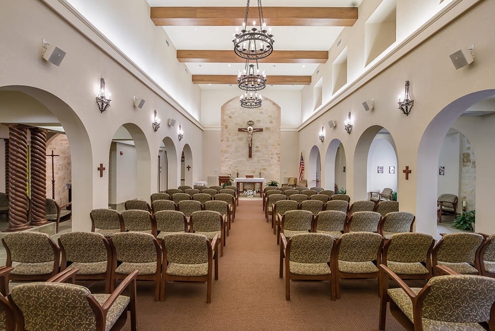 An elegant chapel interior with rows of seating and a central cross at the altar.