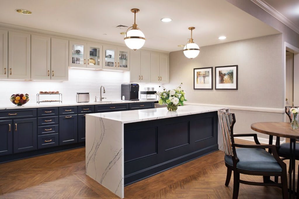 A modern kitchen featuring a large island with a quartz countertop, pendant lighting, white and dark cabinetry, and hardwood flooring.