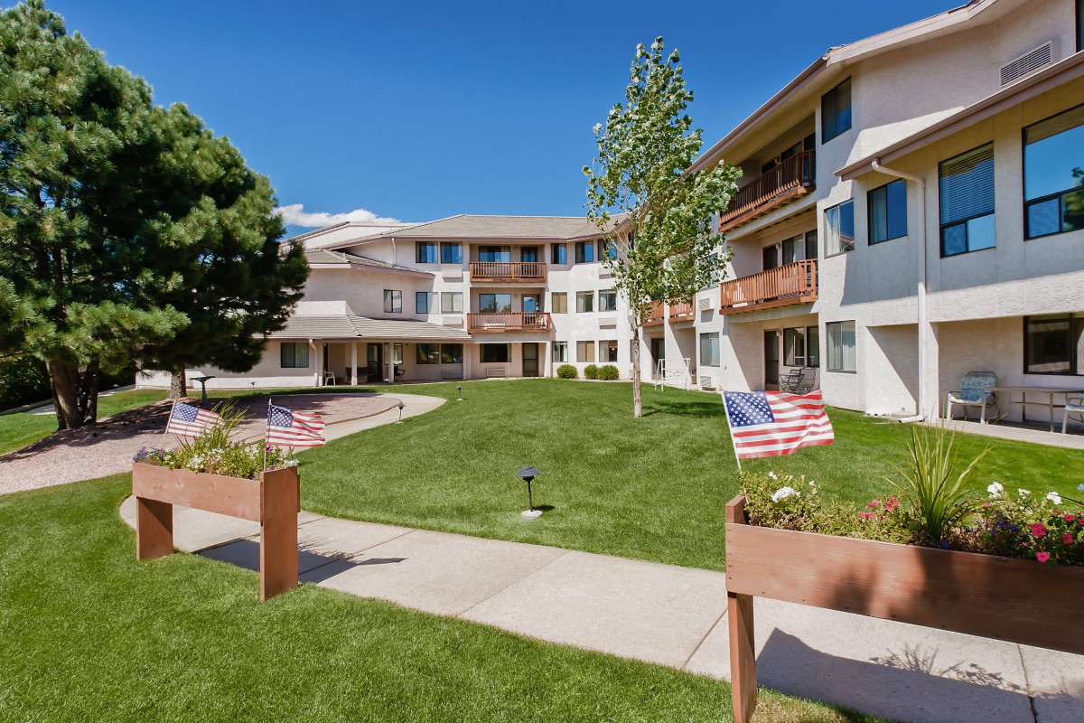 A sunny day in a courtyard of an apartment building with well-maintained grass and small American flags along the walkway.