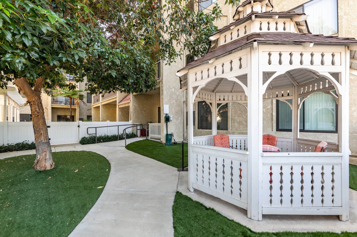 A charming white gazebo sits beside a winding pathway, surrounded by lush greenery.