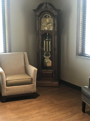 A cozy corner featuring a stylish armchair and an elegant grandfather clock, illuminated by natural light.