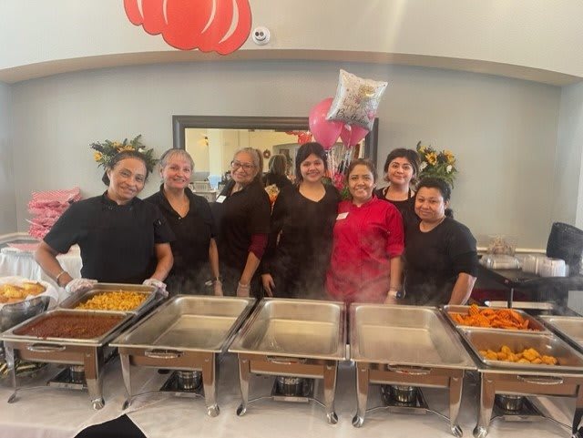 A group of catering staff smiling in front of a buffet setup at an event.