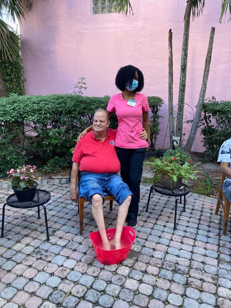 A person receives a foot bath while sitting outdoors on a patio with plants nearby.