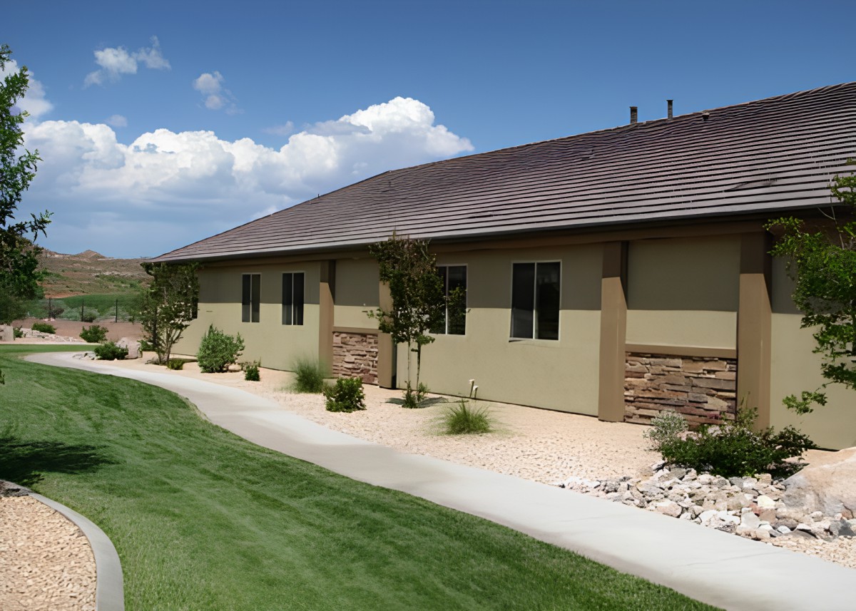 A modern building with a landscaped lawn and sidewalk under a blue sky with scattered clouds.
