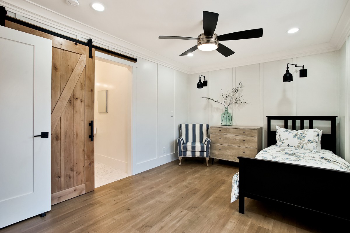 A modern bedroom featuring a barn door, wooden flooring, and minimalist decor.