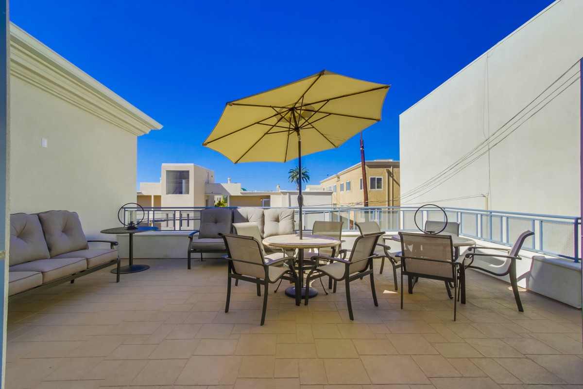 A sunny outdoor patio with a large umbrella, chairs, and tables in an urban setting.