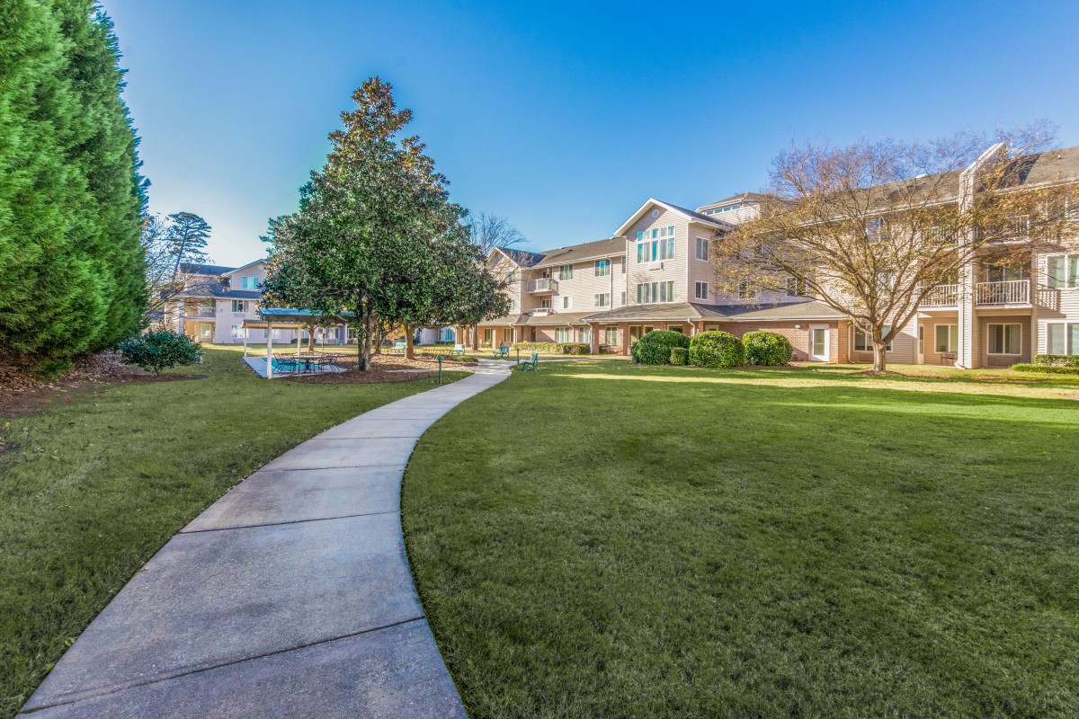A scenic view of a residential building with a well-maintained lawn and surrounding trees.