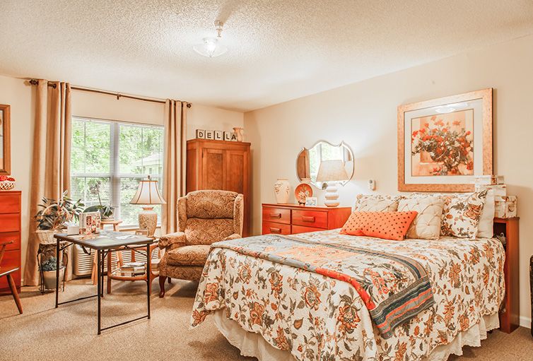 A cozy bedroom with vintage-style decor, featuring a quilted bed, armchair, and wooden furniture.