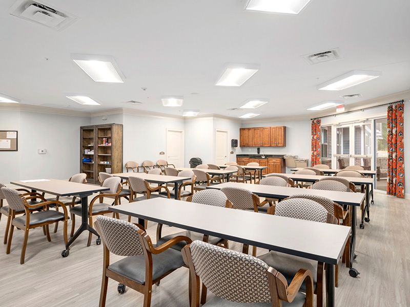 A bright and spacious conference room featuring multiple tables and chairs, with a small kitchen area in the background.