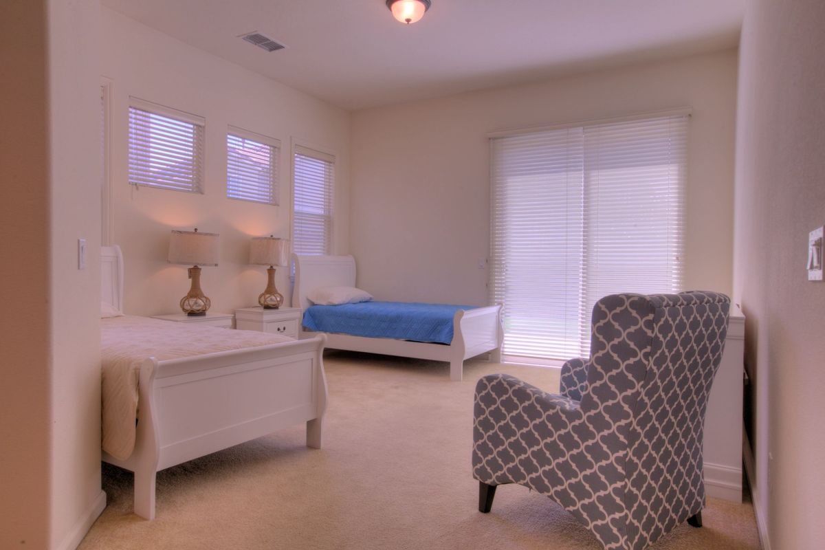 A spacious bedroom with two beds, an armchair, and soft lighting from table lamps.