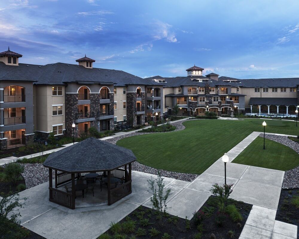 A residential apartment complex with a well-maintained courtyard and gazebo under an evening sky.
