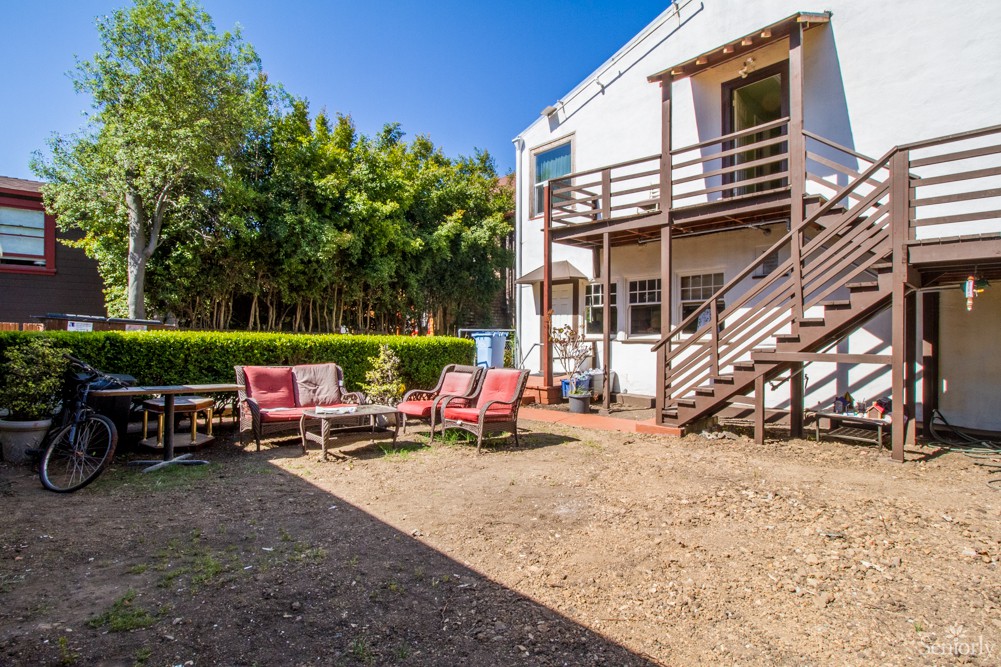 A spacious backyard featuring outdoor seating and a wooden deck with stairs.