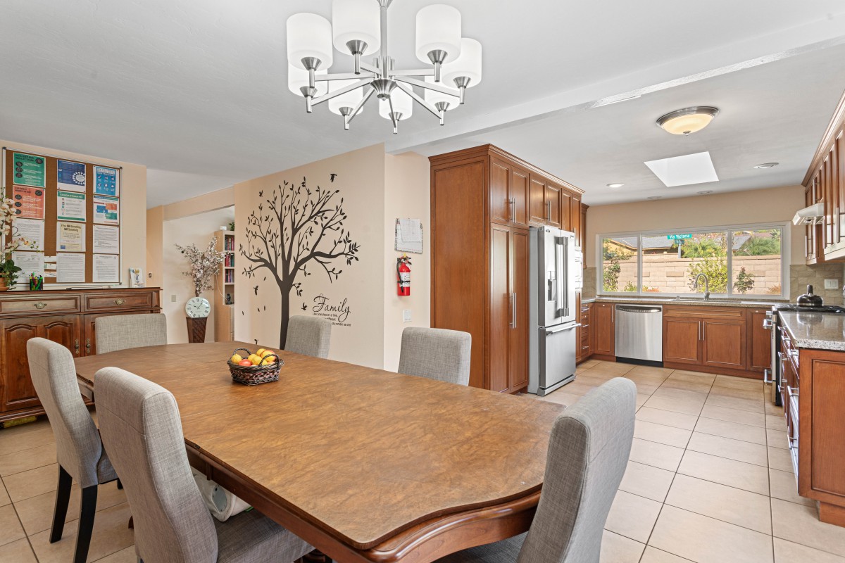 A modern open-concept dining and kitchen area featuring a wooden table, upholstered chairs, and a decorative wall mural.
