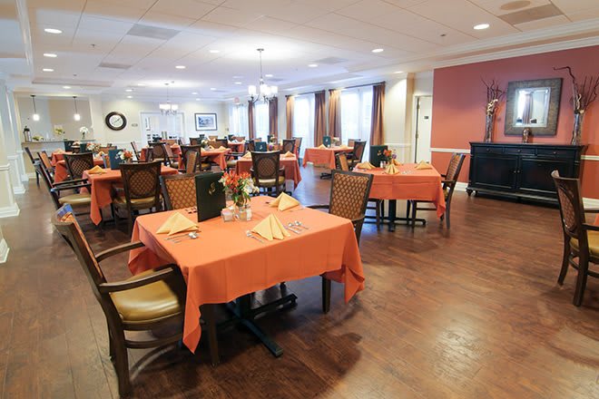 A spacious dining room featuring neatly set tables with orange tablecloths.