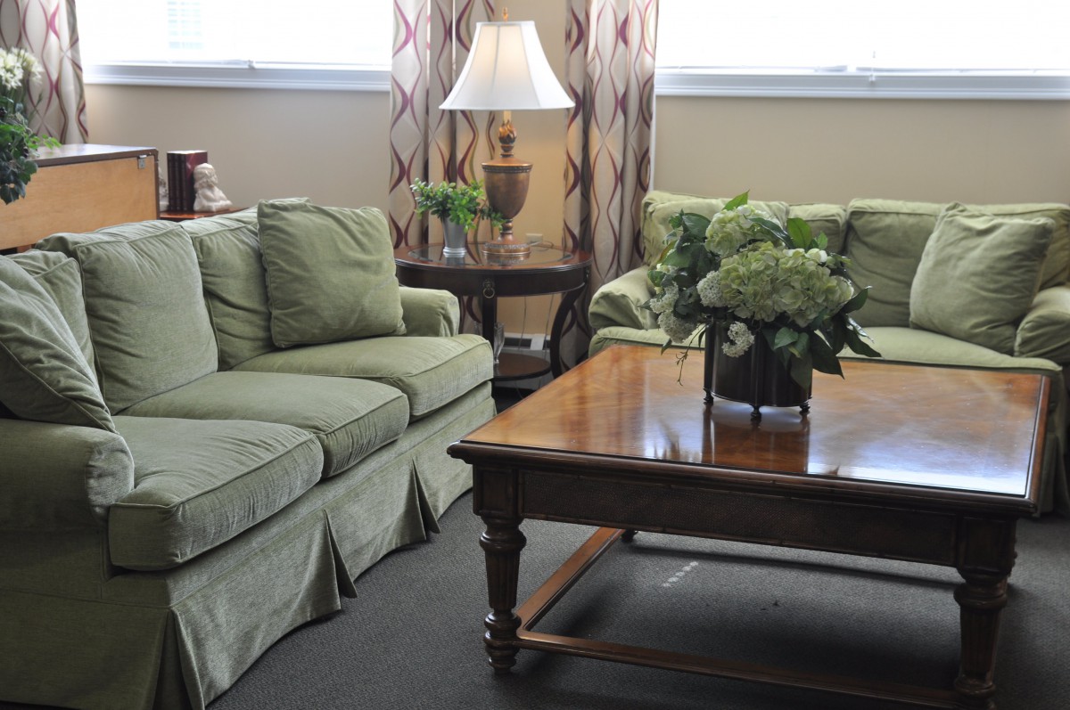 A cozy living room with green sofas and a wooden coffee table adorned with flowers.