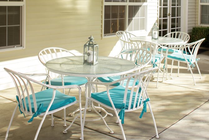 A sunlit patio with a white metal dining set featuring turquoise cushions and a decorative lantern on the table.