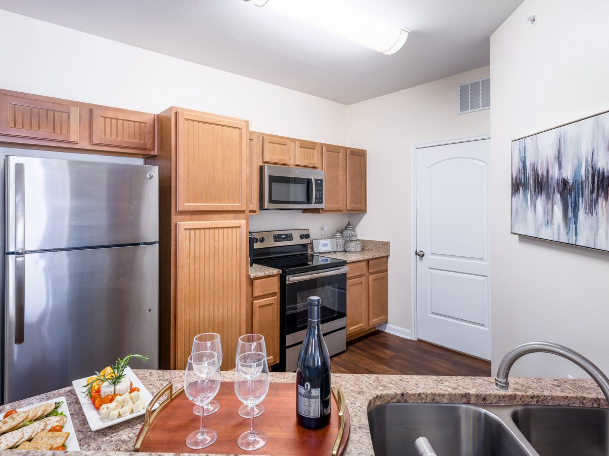 A modern kitchen with wooden cabinets, stainless steel appliances, and a countertop set with wine glasses and a bottle.