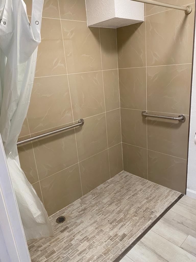 A tiled shower area with grab bars and a curtain.