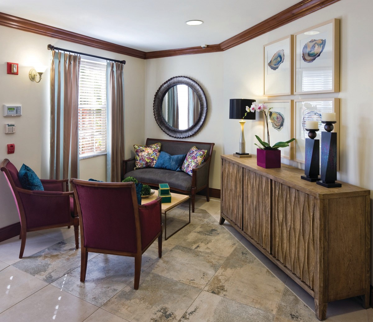 A well-decorated living room featuring a sofa, two chairs, a round mirror, and a wooden cabinet with artistic decorations.
