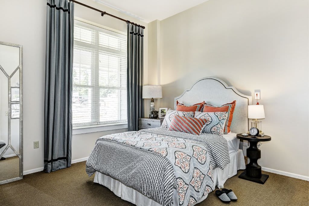 A cozy bedroom with a neatly made bed, decorative pillows, and large window with curtains.