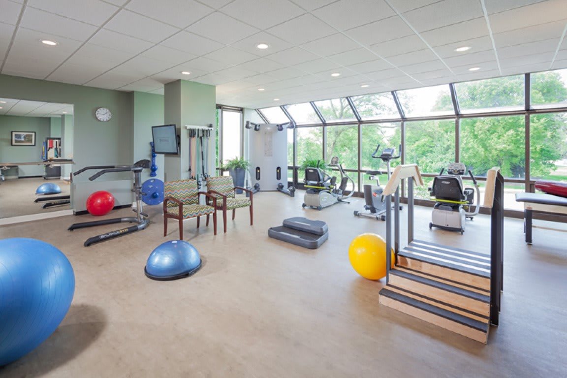 A well-lit gym with various exercise equipment and large windows.