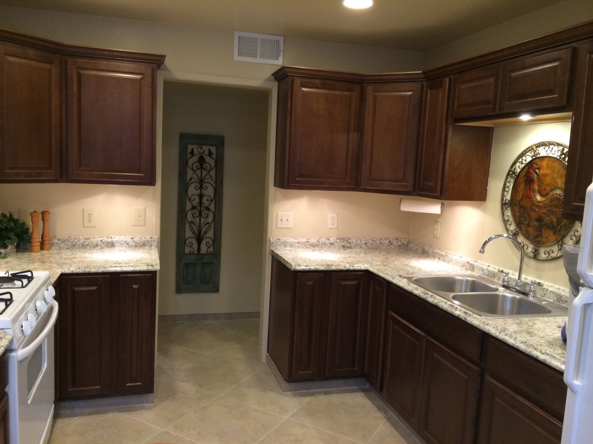 A well-lit kitchen featuring dark wood cabinets and a dual sink, with light countertops.